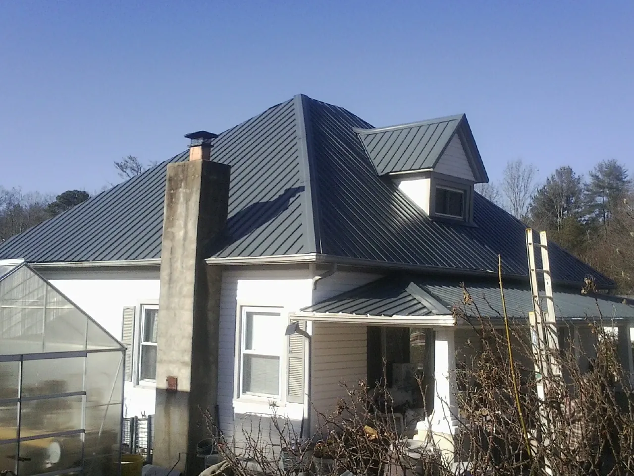 Dark blue standing seam metal roof on a white farmhouse with dormer — Slate & Tile Roof Repair by Roofing Brothers in Altamahaw