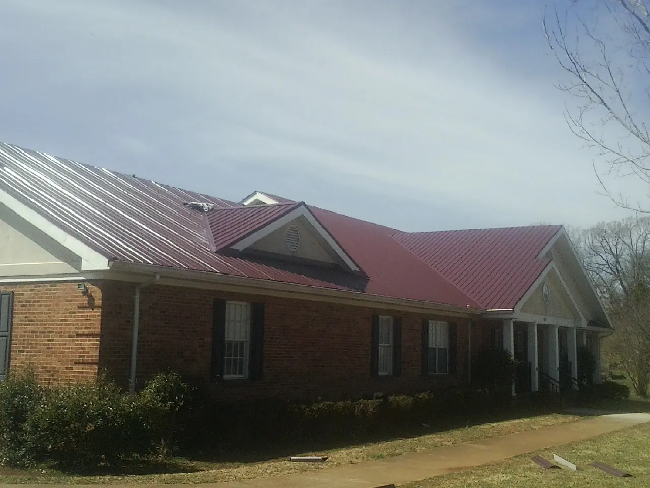 Red metal roof with gabled entries on a long brick building, from a Hail Damage Roof Repair job in Altamahaw