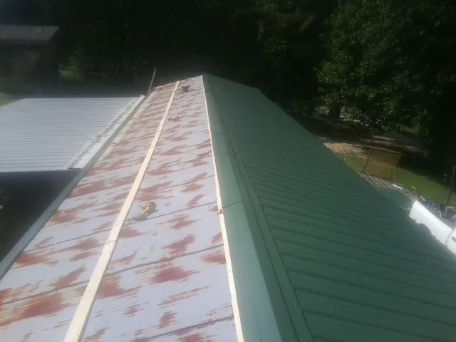Old rusted panels beside newly installed green metal roofing — Wind Damage Roof Repair by Roofing Brothers in Altamahaw
