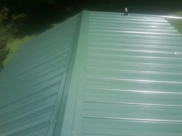 New green metal panels meeting at the ridge of a roof — Flat Roof Repair work by our crew in Altamahaw