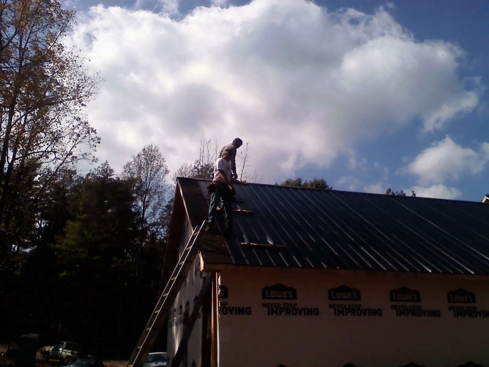 Roofer fastening dark metal panels high against a cloudy sky, from a Roof Inspection job in Altamahaw