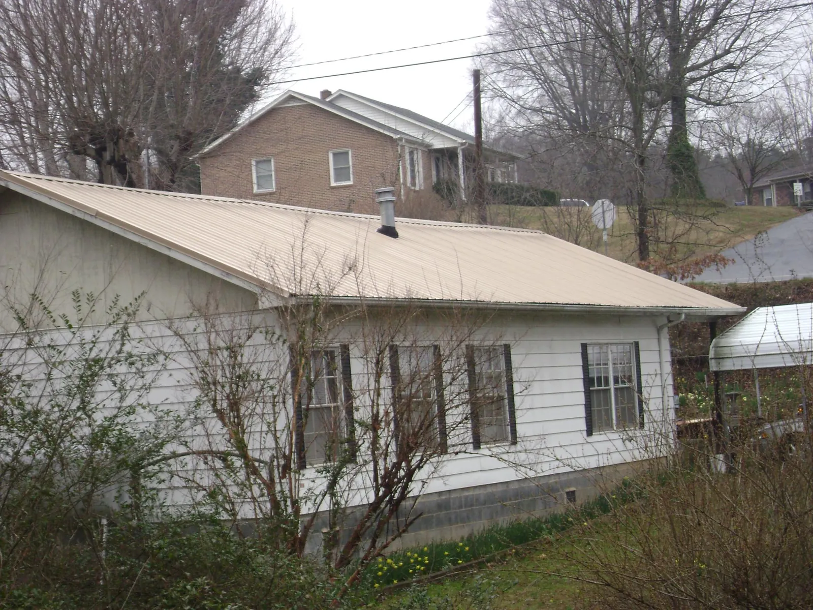 Tan metal roof on a white sided house set into a hillside — Commercial Roofing by Roofing Brothers in Altamahaw