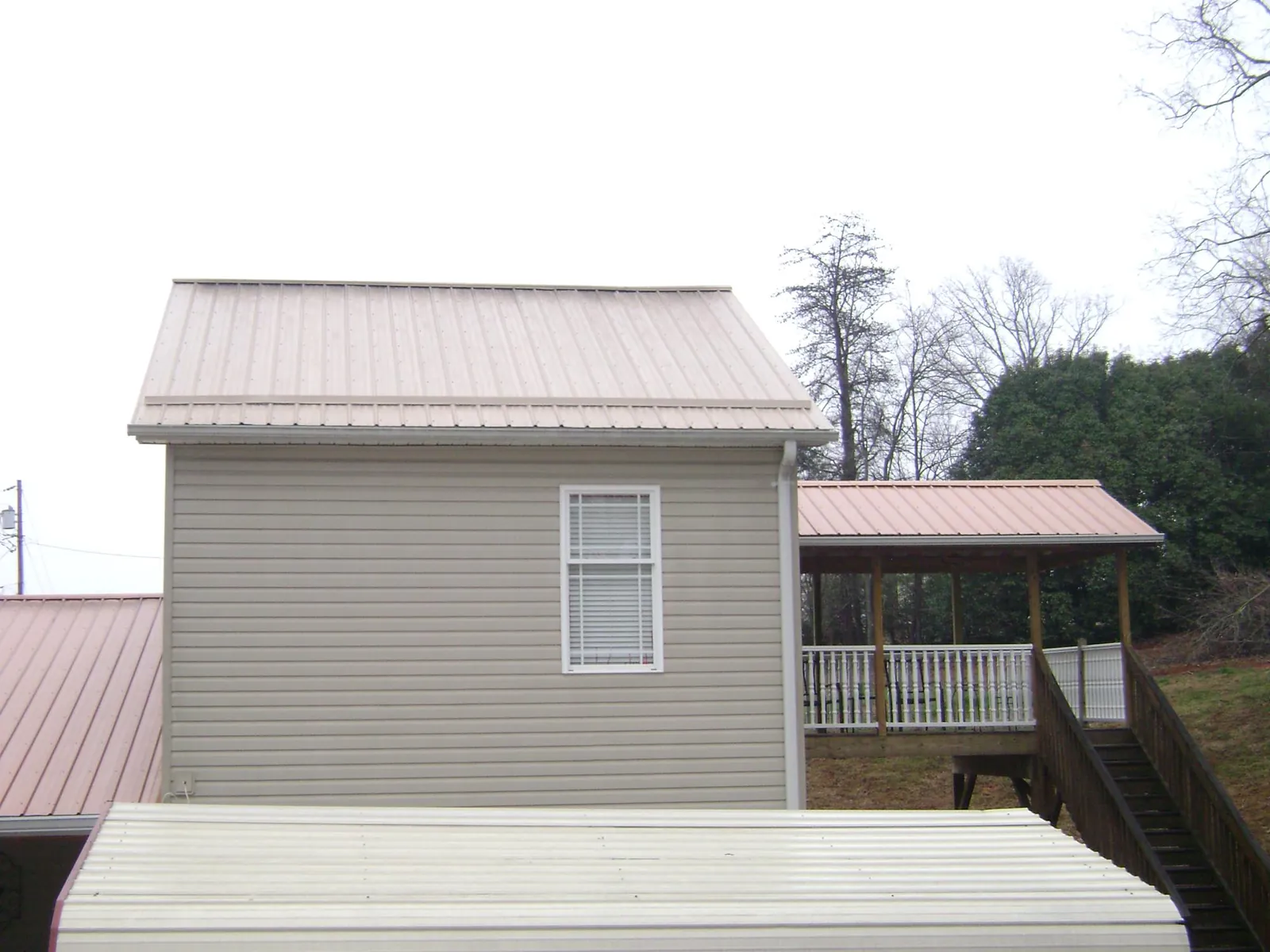 Tan metal roofs on a two story addition and attached porch, from a Roof Replacement job in Altamahaw
